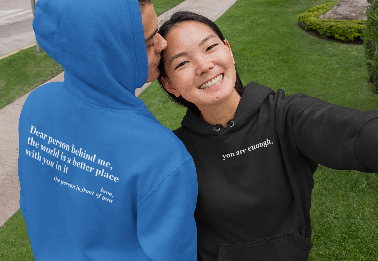 Two people wearing hoodies with motivational quotes, one blue and one black, outdoors.