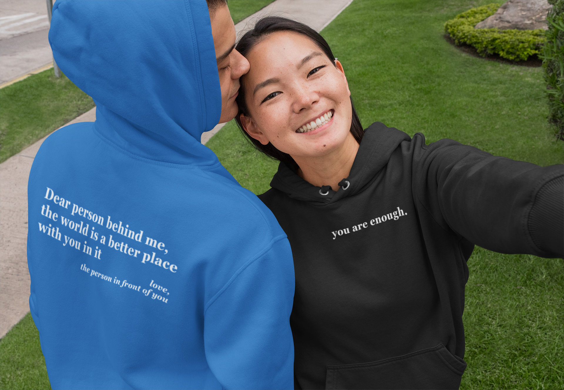 Two people wearing hoodies with motivational quotes, one blue and one black, outdoors.