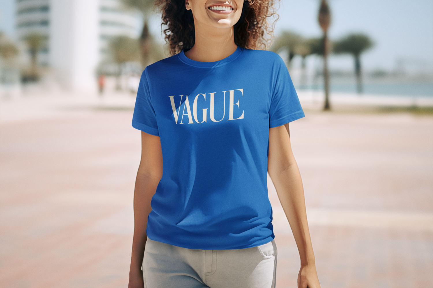 Woman wearing a royal blue graphic t-shirt that says “VAGUE” in white serif letters, smiling outdoors.
