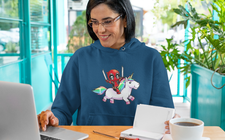 woman working behind a laptop wearing a navy blue hoodie with a graphic of deadpool on a unicorn