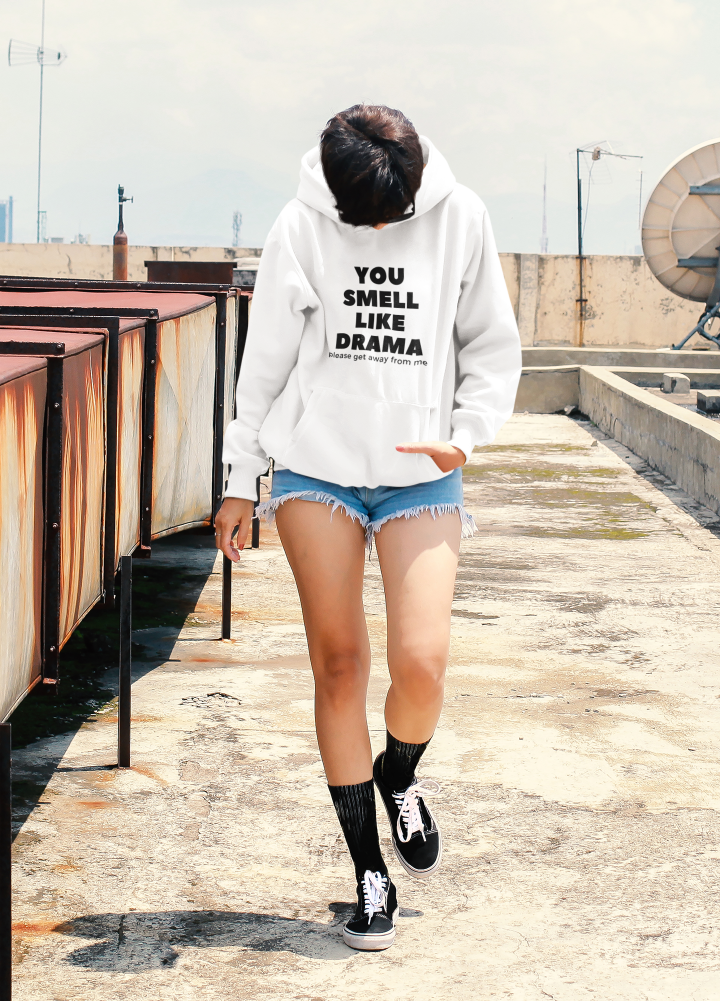 woman walking head down in a white hoodie with the words you smell like drama please get away from me