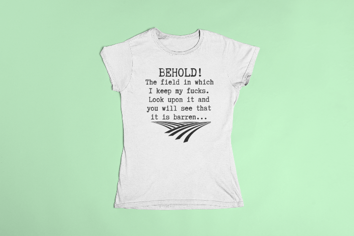 a white t shirt laid flat that says behold! The field in which I keep my fucks. Look upon it and you will see that it is barren...