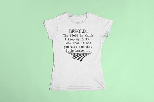 a white t shirt laid flat that says behold! The field in which I keep my fucks. Look upon it and you will see that it is barren...